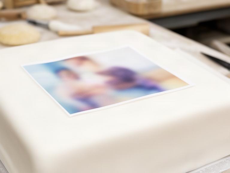 Tarta de fondant blanca en un obrador de Zafra con una fotografía comestible colocada sobre la superficie